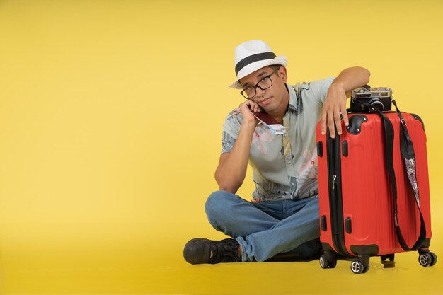 Jeune touriste masculin assis sur le sol avec sa valise attendant son vol pour arriver