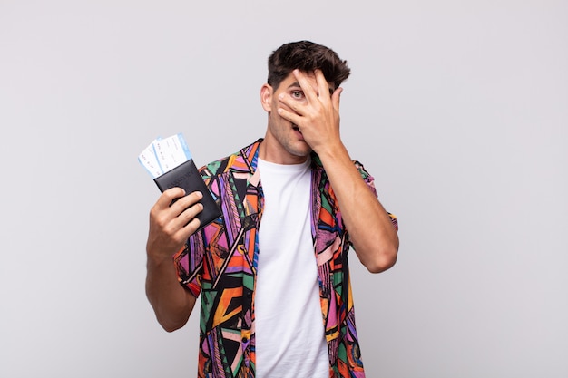 Jeune touriste avec un passeport l'air choqué, effrayé ou terrifié, couvrant le visage avec la main et jetant un œil entre les doigts