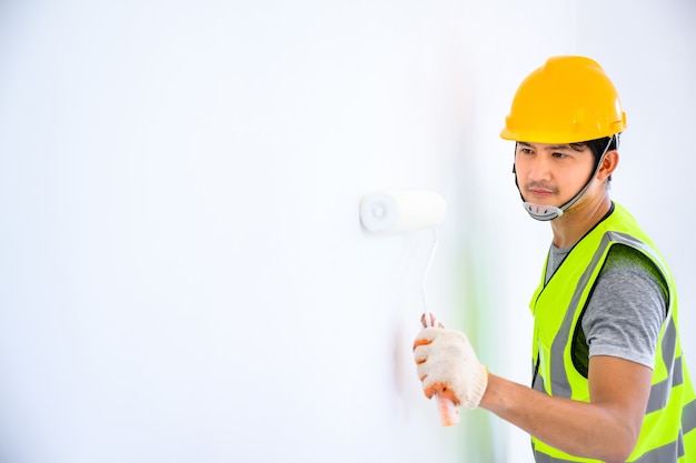 jeune travailleur asiatique En tant que peintre pour peindre les murs de la maison et utiliser un rouleau pour peindre l'apprêt blanc sur le chantier de construction