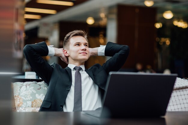 Jeune travailleur ayant une pause et se reposer après avoir résolu la tâche, vêtu d'un costume noir au centre commercial