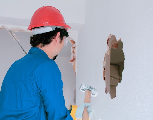 jeune travailleur avec un casque de protection rouge et portant un costume bleu chaudière. concept de démolition