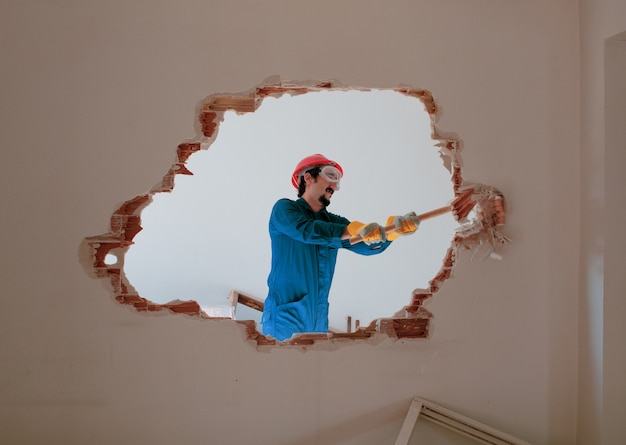 Photo jeune travailleur avec un casque de protection rouge et portant un costume bleu chaudière. concept de démolition