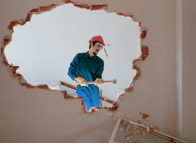 Photo jeune travailleur avec un casque de protection rouge et portant un costume bleu chaudière. concept de démolition