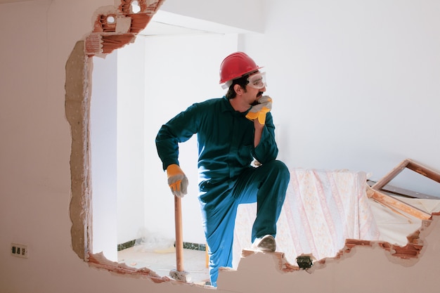 Photo jeune travailleur avec un casque de protection rouge et portant un costume bleu chaudière. concept de démolition