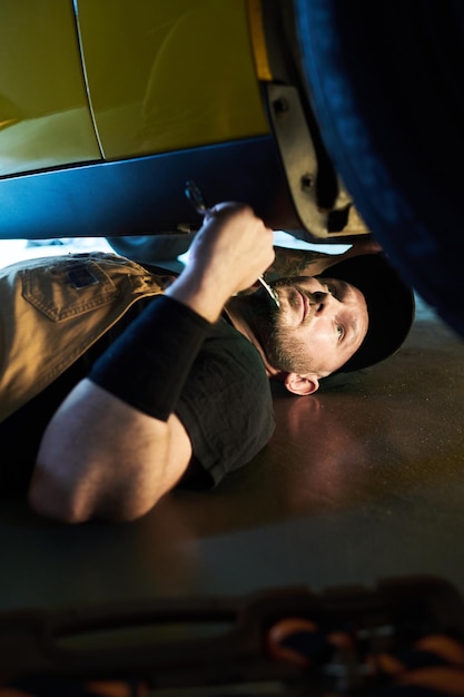 Jeune travailleur du service de maintenance allongé sur le sol sous une voiture cassée