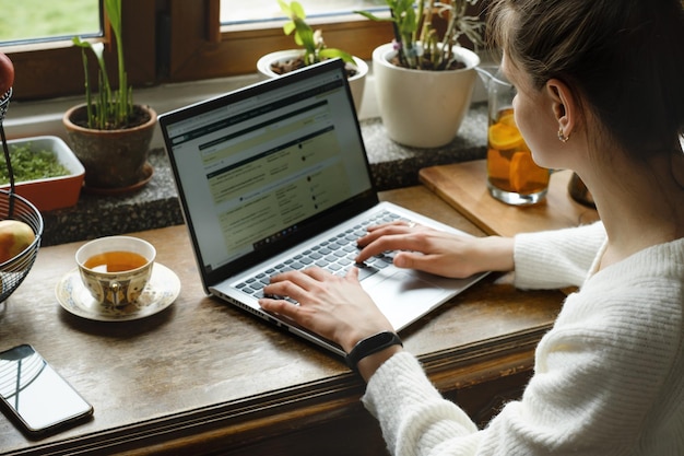 Jeune travailleur indépendant sur un ordinateur portable à la maison femme utilisant l'ordinateur dans la cuisine pour le travail à distance