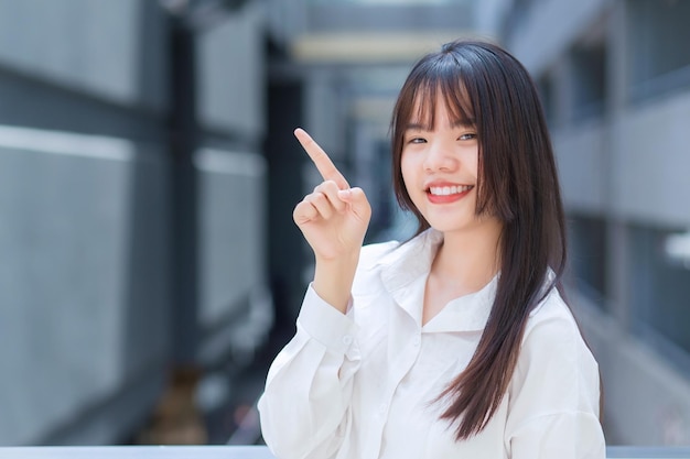 Une jeune travailleuse asiatique professionnelle qui porte une chemise blanche pointe la main pour présenter quelque chose.