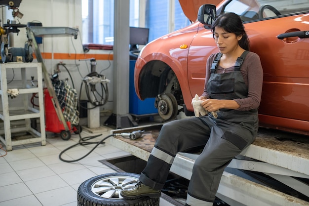 Jeune travailleuse fatiguée du service d'entretien automobile enlevant des gants