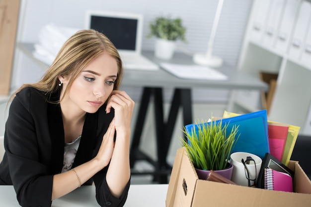 Jeune travailleuse licenciée au bureau assis près d'une boîte en carton avec ses effets personnels. Être viré concept.