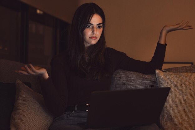 Une jeune travailleuse malheureuse regarde l'écran de son ordinateur portable, choquée par la panne d'un appareil ou par des problèmes opérationnels tard dans la nuit. Une femme frustrée, confuse, surprise par une erreur inattendue sur un appareil informatique.