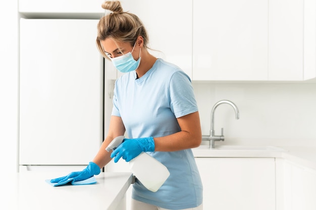 Jeune travailleuse portant un masque de prévention et des gants pendant le nettoyage de l'appartement