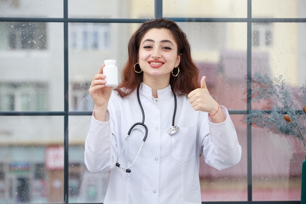 Une jeune travailleuse de la santé tenant une capsule de médicament et un geste du pouce vers le haut Photo de haute qualité
