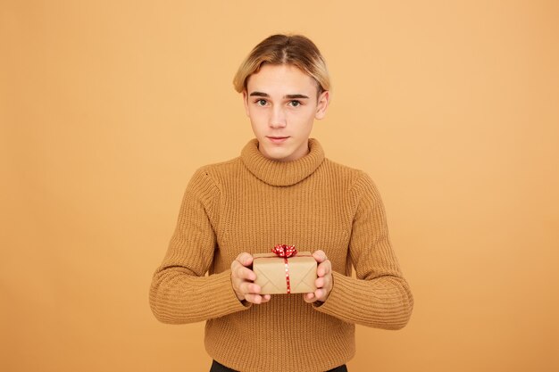 Le jeune type blond tient un cadeau de Noël dans ses mains sur le fond beige dans le studio