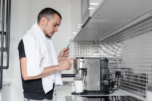 Un jeune va travailler le matin. Se brosse les dents près d'une machine à café en attendant une tasse de café