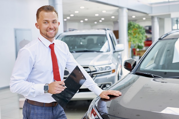 Jeune vendeur caucasien confiant discuter de l'automobile avec les acheteurs