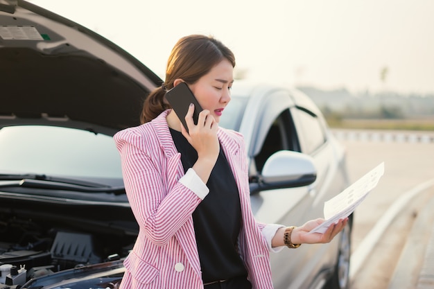 Photo jeune vendeuse asiatique écrivant sur presse-papiers avec voiture cassée