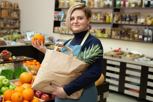 Jeune vendeuse recueille des légumes et des fruits dans un sac en papier