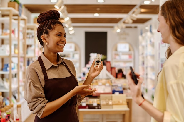 Jeune vendeuse souriante donnant des conseils au client sur le parfum dans un magasin de cosmétiques