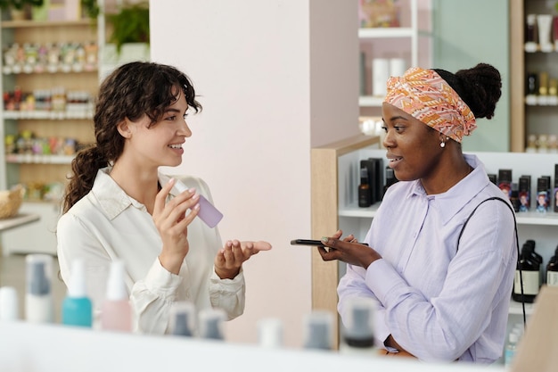 Jeune vendeuse souriante recommandant un produit cosmétique pour femme noire