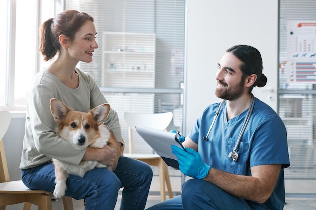 Jeune vétérinaire mâle avec document médical parlant au propriétaire de l'animal