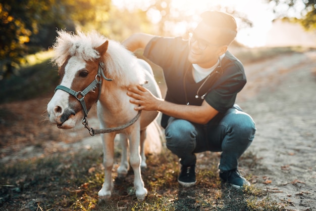 Jeune vétérinaire masculin séduisant examinant et nourrissant un adorable petit cheval poney.