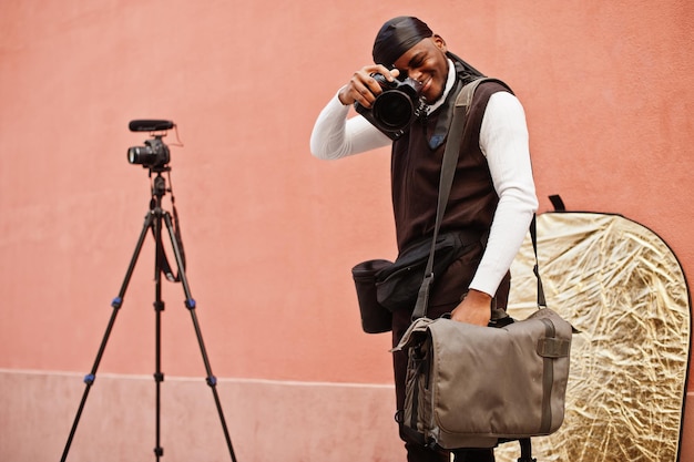 Jeune vidéaste afro-américain professionnel tenant une caméra professionnelle avec un équipement professionnel Caméraman afro portant du duraq noir faisant une vidéo