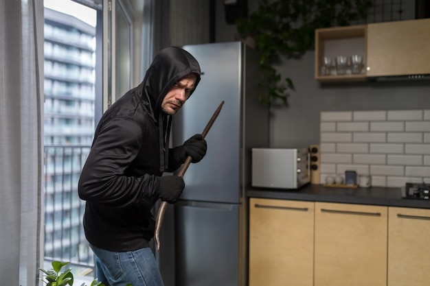 Un jeune voleur en vêtements sombres entre avec précaution et en silence par la fenêtre du balcon dans l'immeuble.