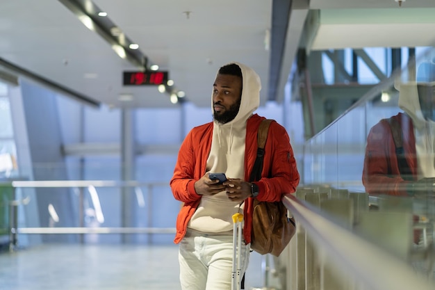 Jeune voyageur africain du millénaire utilisant un téléphone portable en attendant son vol à l'aéroport