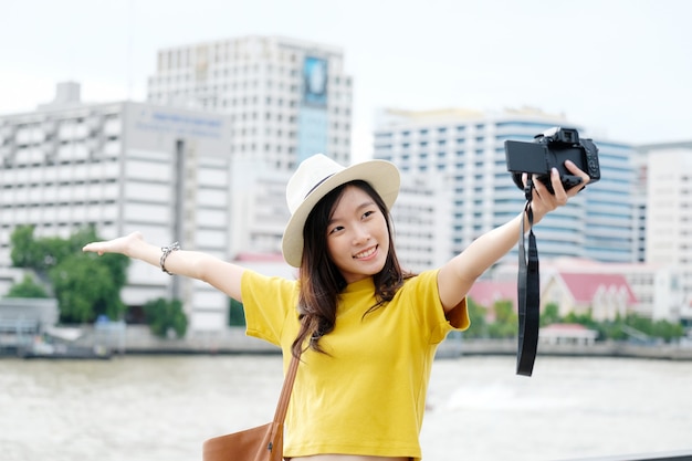 Jeune voyageur asiatique femme mignonne dans un style décontracté faisant selfie caméra dans le fond de la ville urbaine