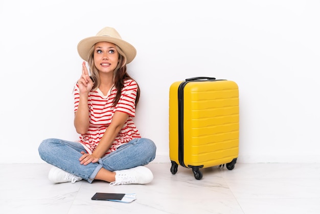 Jeune voyageur fille assise sur le sol isolé sur fond blanc avec les doigts croisés et souhaitant le meilleur