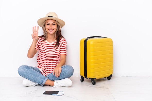 Jeune voyageur fille assise sur le sol isolé sur fond blanc heureux et comptant trois avec les doigts