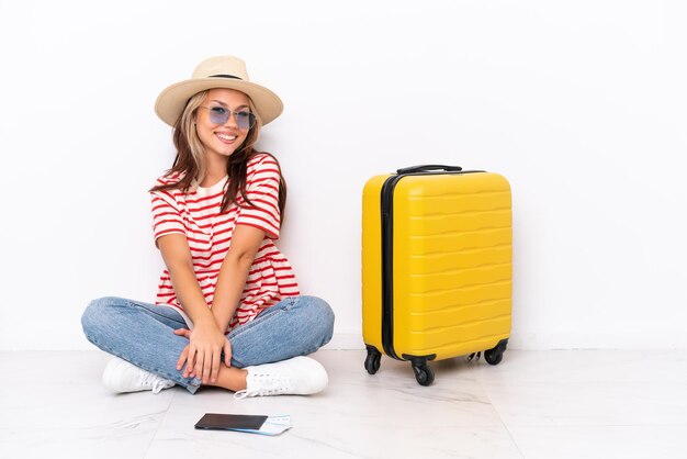 Jeune voyageur fille assise sur le sol isolé sur fond blanc avec des lunettes et souriant