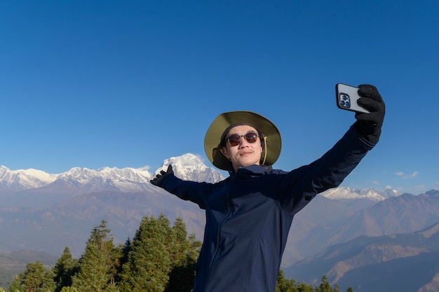 Un jeune voyageur prend un selfie ou un appel vidéo en se tenant au sommet d'une montagne