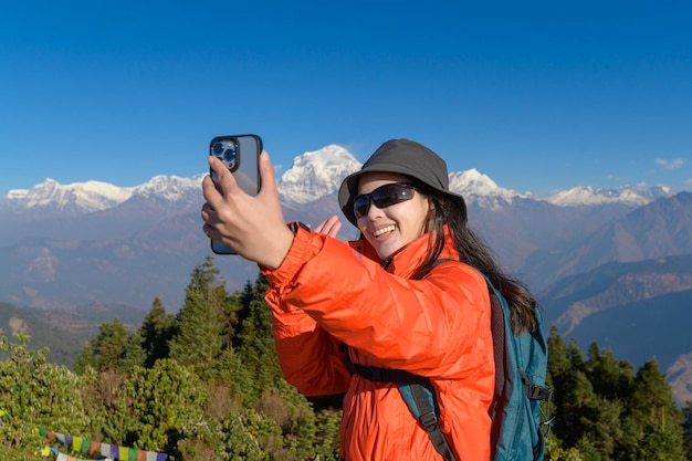 Un jeune voyageur prend un selfie ou un appel vidéo en se tenant au sommet d'une montagne