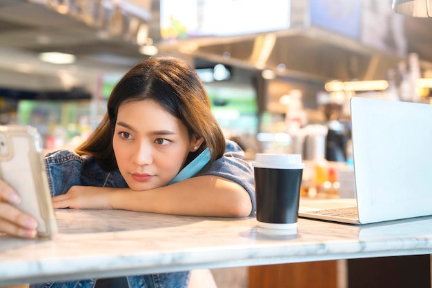 Jeune voyageuse asiatique femme s'asseoir se détendre l'expression du visage main utiliser un smartphone en attente de temps à bord dans un café-restaurant au terminal de départ de l'aéroport