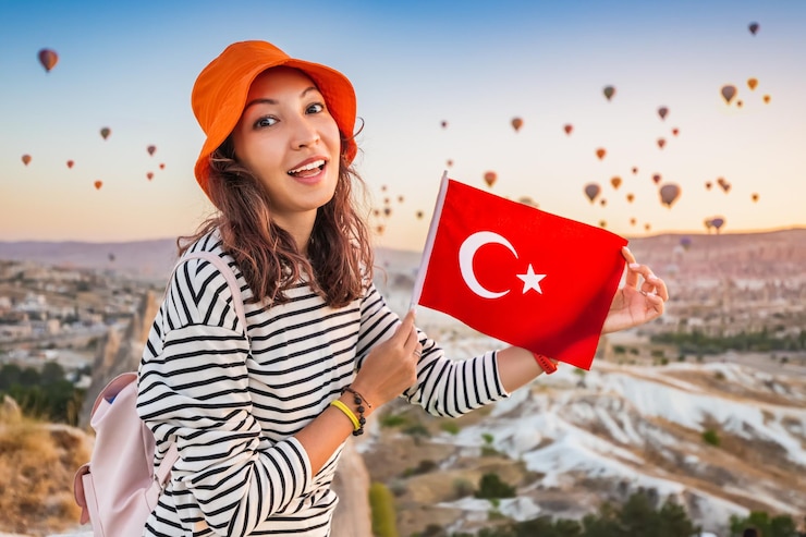 Photo une jeune voyageuse avec un drapeau turc sur un point de vue admire le paysage grandiose de nombreux ballons à air au-dessus de la vallée de la cappadoce en turquie