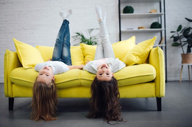 Jeunes adolescents drôles allongé sur le canapé jaune et à la recherche de straigt. Ils sourient. Les filles tiennent les jambes en l'air. Leurs cheveux touchent le sol.