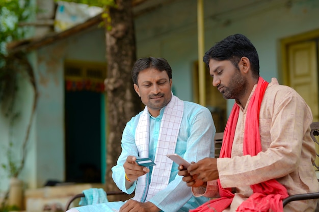 Jeunes agriculteurs indiens utilisant une carte de débit ou de crédit avec un smartphone à la maison