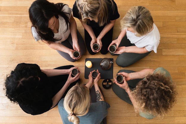 Photo de jeunes amies agenouillées autour d'un plateau tiennent des tasses de thé chaud lors d'une cérémonie du thé