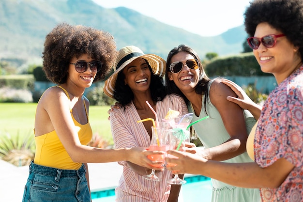 De jeunes amies biraciales heureuses grillent des cocktails tout en s'amusant à la fête au bord de la piscine en été