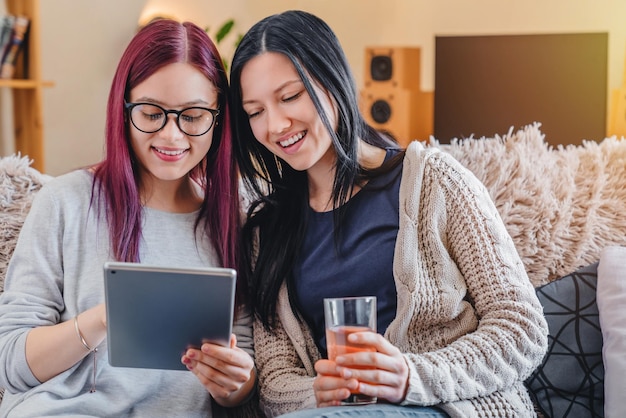 Jeunes amies utilisant une tablette numérique ensemble sur un canapé à la maison