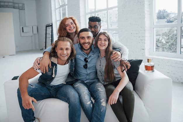 Jeunes amis drôles s'amuser assis sur le canapé à l'intérieur blanc