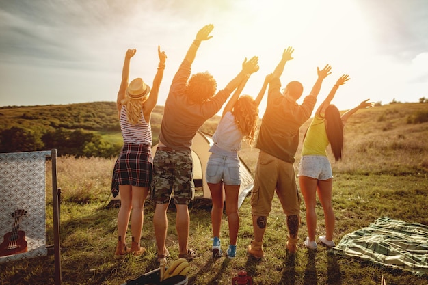 De jeunes amis heureux profitent d'une journée ensoleillée dans la nature. Ils regardent le soleil et se saluent, heureux d'être ensemble.