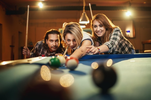 De jeunes amis joyeux et souriants jouent au billard au bar après le travail. Ils participent à des activités récréatives.