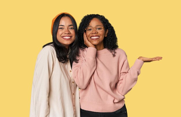 Jeunes amis latins ensemble dans le studio tient l'espace de copie sur une paume garder la main sur la joue étonné