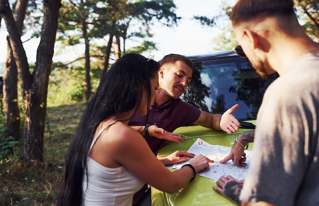 Jeunes amis lisant une carte qui se trouve sur le capot d'une jeep verte moderne dans la forêt.