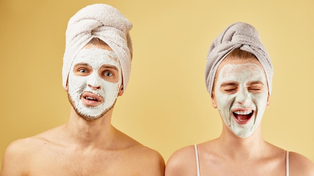 Jeunes amis mec et fille avec une serviette d'émotions expressives drôles sur la tête et le masque facial isolés sur un concept de soins de la peau de fond jaune
