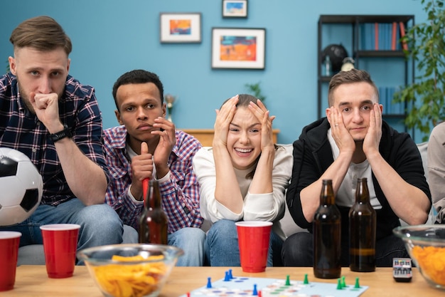 Jeunes amis multiraciaux regardant un match de football à la télévision ensemble à la maison et déçus de leur