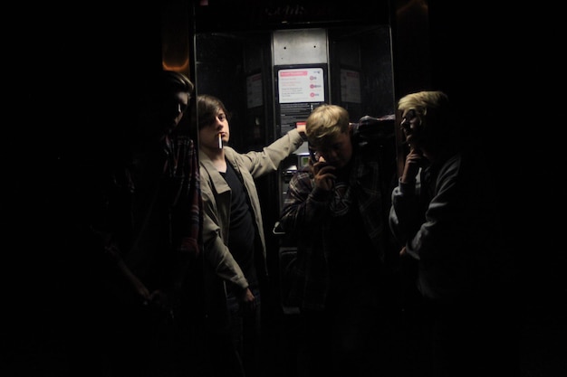Photo des jeunes amis près d'une cabine téléphonique la nuit.