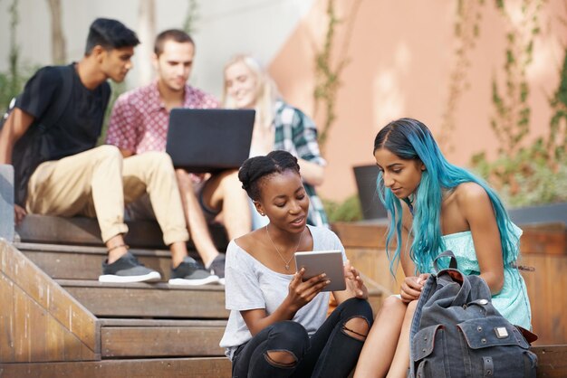 Photo des jeunes amis utilisant un ordinateur portable et une tablette assis sur des marches